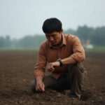 Young man planting a seedling in a rural field for future home growth.